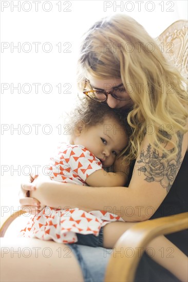 Mother sitting on chair and embracing daughter (12-17 months)