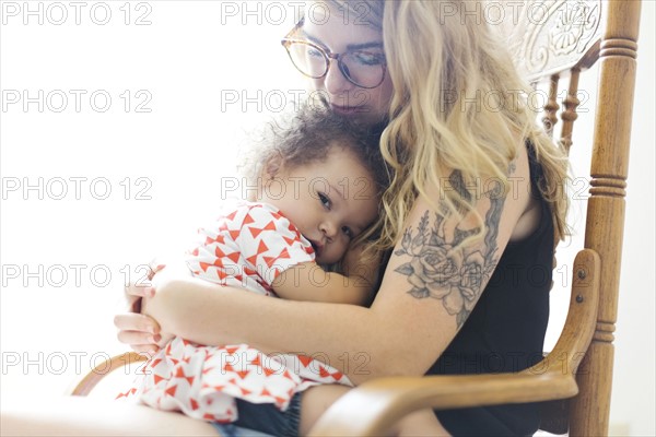 Mother sitting on chair and rocking daughter (12-17 months)