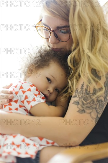 Mother sitting on chair and embracing daughter (12-17 months)