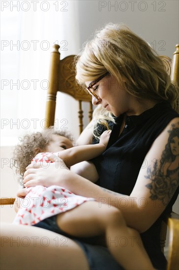 Mother sitting on chair and breastfeeding daughter (12-17 months)