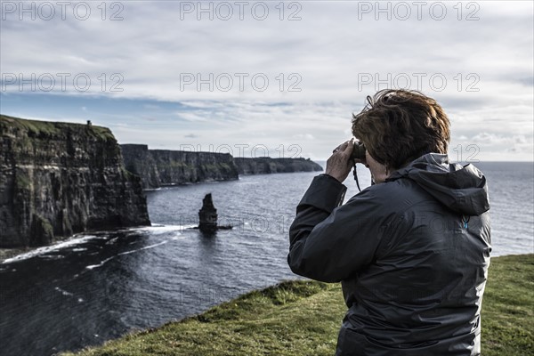 Ireland, Clare County, Woman looking through binoculars on Cliffs of Moher