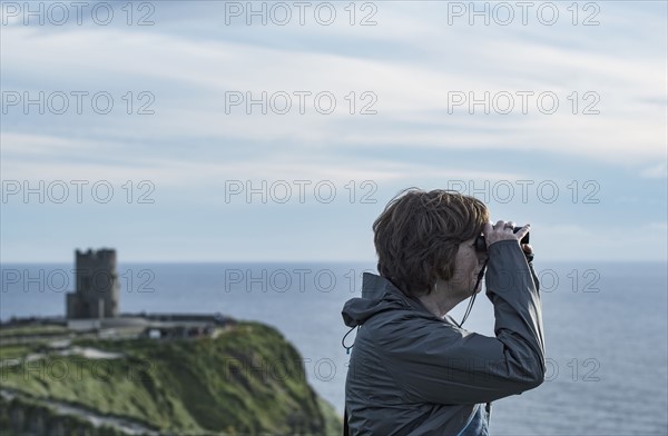 Ireland, Clare County, Woman looking through binoculars on Cliffs of Moher