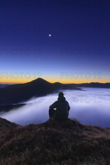 Ukraine, Zakarpattia region, Rakhiv district, Carpathians, Chornohora, Tourist sitting on mountain meadow at dusk