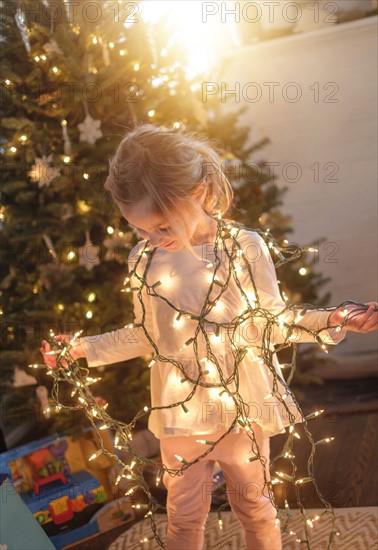 Little girl (4-5) wrapped with christmas lights in living room