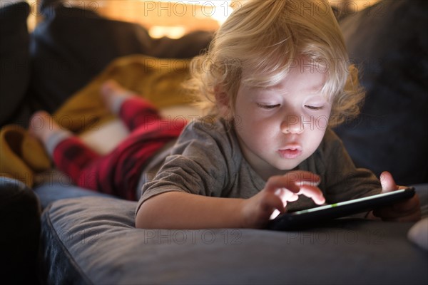 Little boy (2-3) lying on front and playing game on smart phone