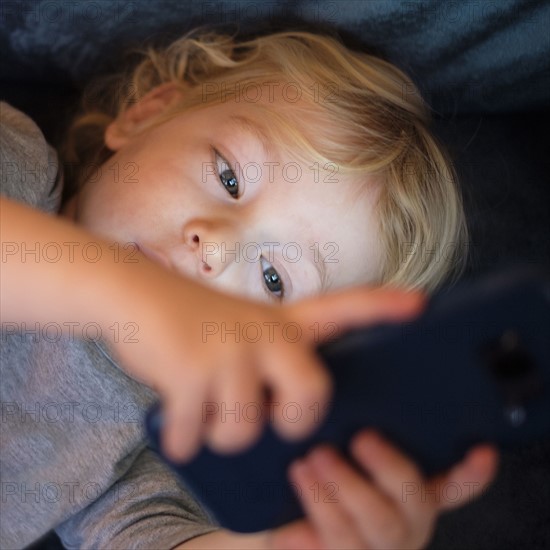 Little boy (2-3) lying down and playing game on smart phone