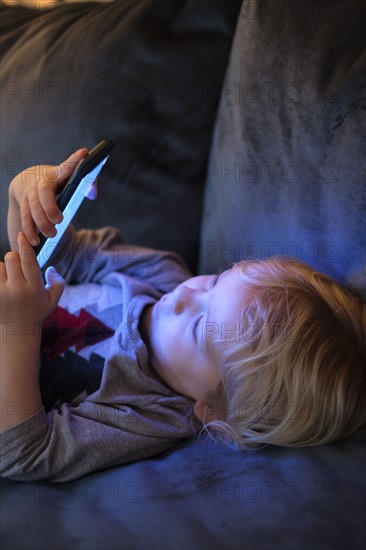 Little boy (2-3) lying down and playing game on smart phone