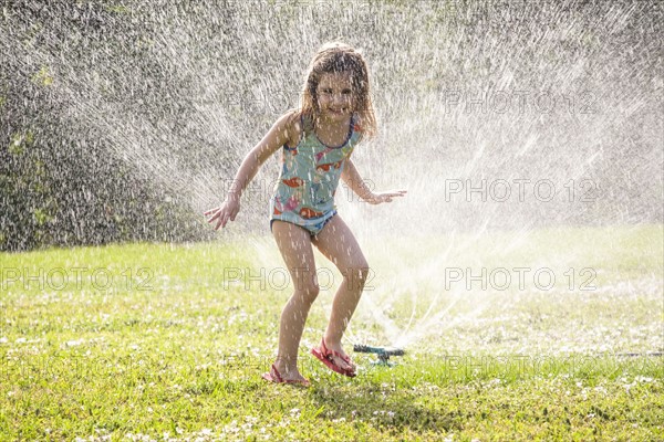 Girl (4-5) splashing in sprinkler water on lawn