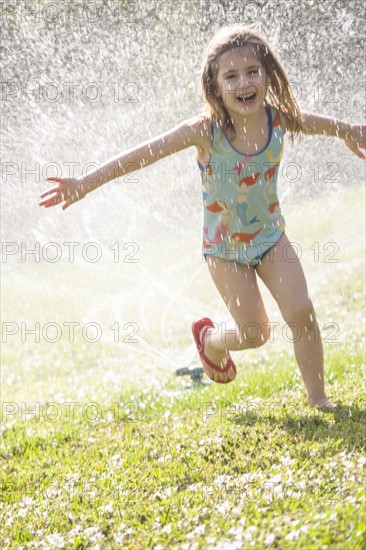 Girl (4-5) splashing in sprinkler water on lawn