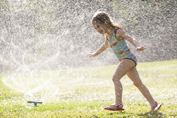 Girl (4-5) splashing in sprinkler water on lawn