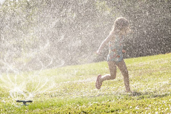 Girl (4-5) splashing in sprinkler water on lawn