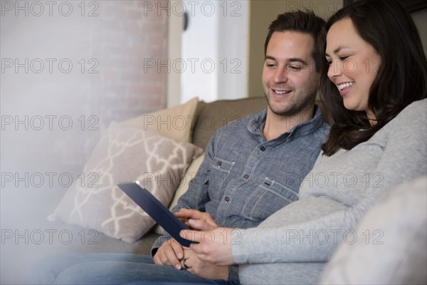 Mid adult couple sitting on sofa and using tablet pc