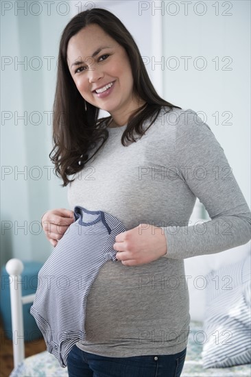 Pregnant woman holding infant bodysuit in bedroom