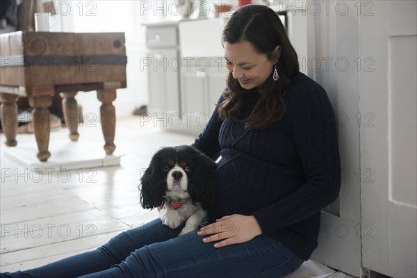 Pregnant woman sitting on floor and holding dog