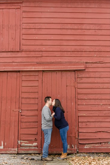 Couple kissing in front of red barn