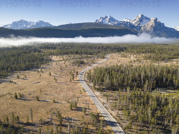 USA, Idaho, Sawtooth Range, Road in forest with snowcapped mountains in background