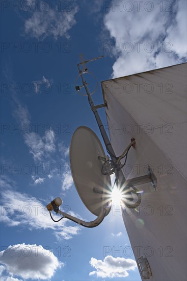 Sun shining through space between satellite dish and facade