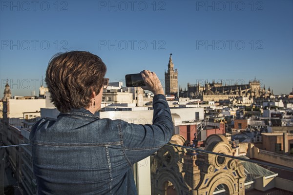 Spain, Andalusia, Seville, Plaza Nueva, Woman taking photo of cityscape and la Giralda with smartphone