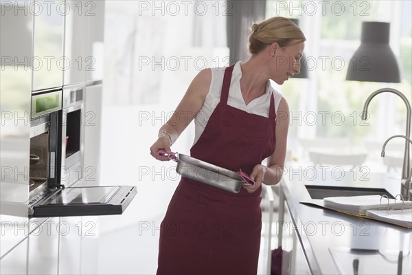 Woman standing with hot baking pan and checking recipe