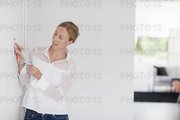 Woman comparing color swatch with white wall