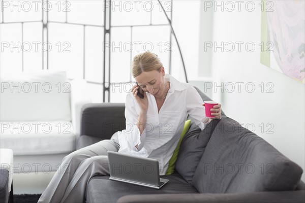 Woman talking on phone and using laptop in living room