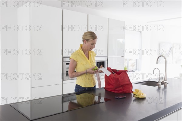 Mature woman unpacking groceries in modern kitchen