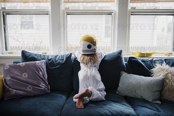 Girl wearing helmet on sofa by window