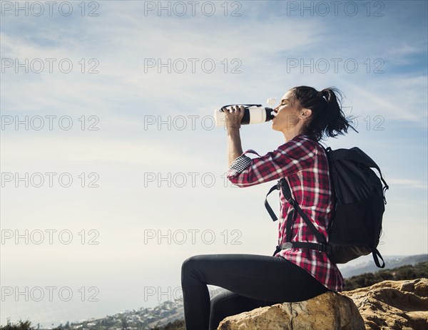 Woman on hike drinking water while sitting on rock