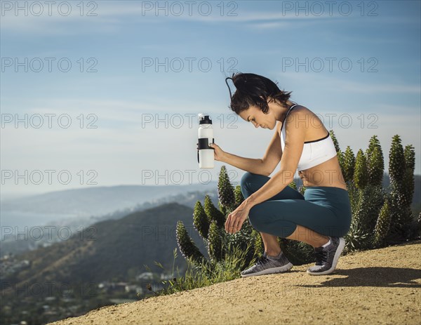 Woman in sportswear crouching with water bottle