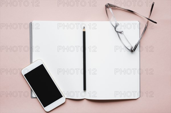 Smart phone, pencil and glasses on open notebook