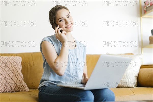 Woman using laptop and smart phone on sofa