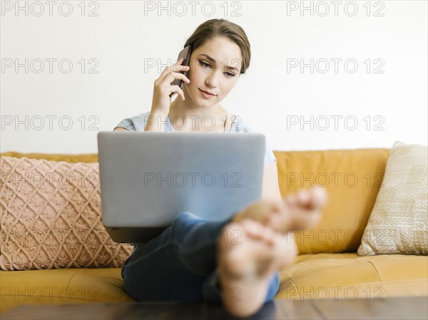 Woman using laptop and smart phone on sofa