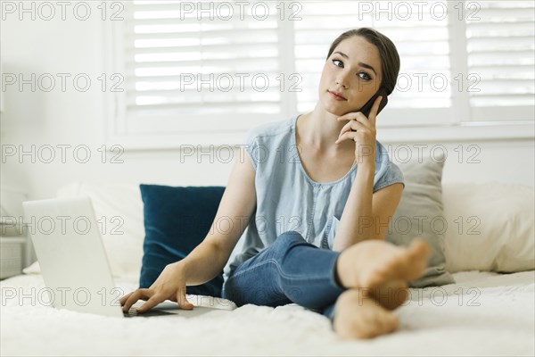 Woman using laptop and smart phone on bed