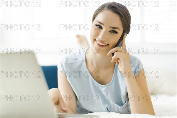 Woman using laptop and smart phone on bed