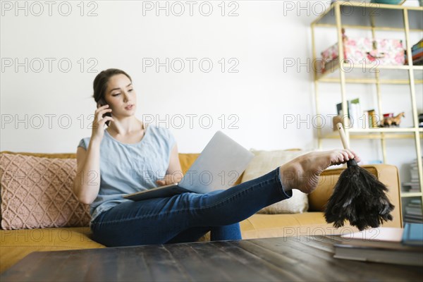 Woman using laptop and smart phone while dusting with foot