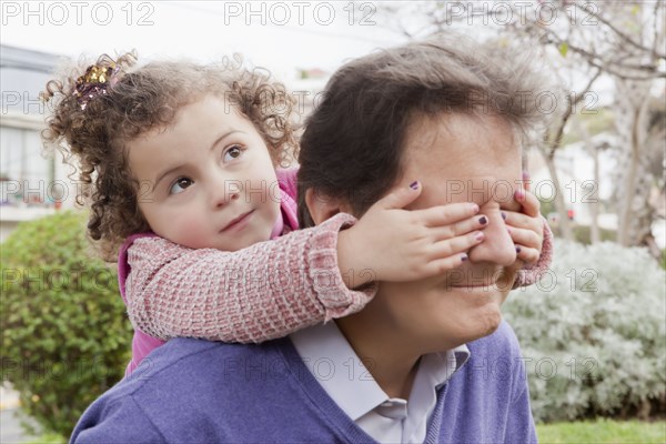 Girl covering father's eyes during piggyback ride