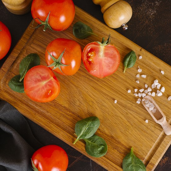 Tomatoes, basil and salt on wooden cutting board