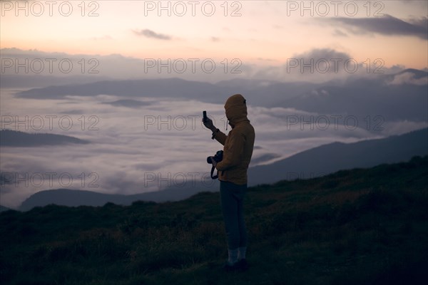 Young man photographing with smart phone at sunset in the Carpathian Mountain Range