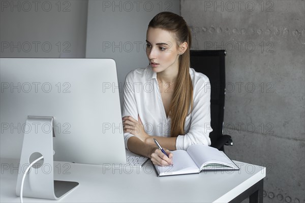 Young businesswoman taking notes while working at desktop computer
