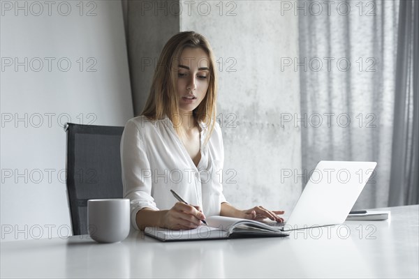 Young businesswoman writing notes while working on laptop