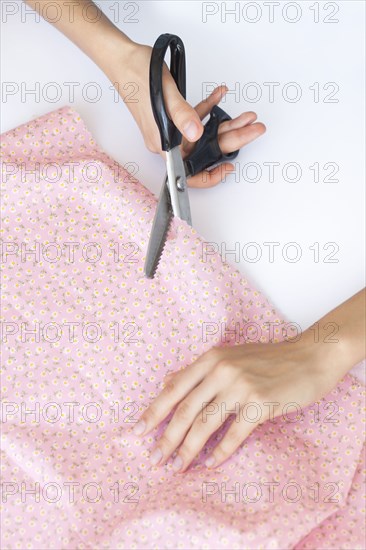 Hands of woman cutting pink floral pattern fabric