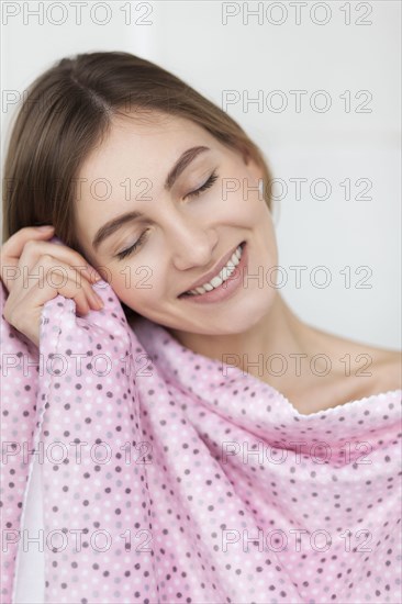 Smiling woman feeling soft fabric on her cheek