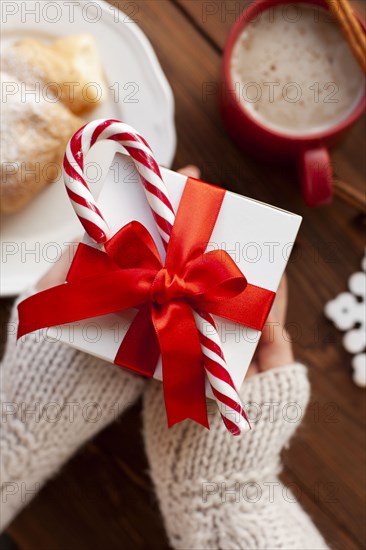 Hands of woman holding Christmas present with candy cane