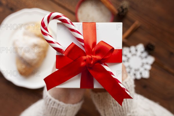 Hands of woman holding Christmas present with candy cane