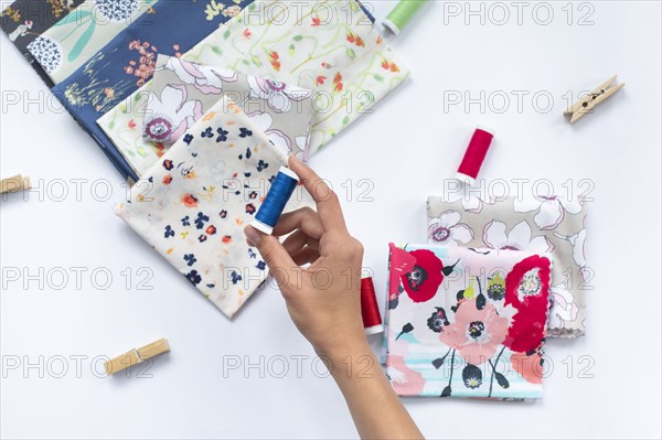 Woman's hand holding blue thread above variety of fabrics