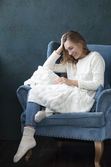 Smiling woman witting in armchair with white blanket