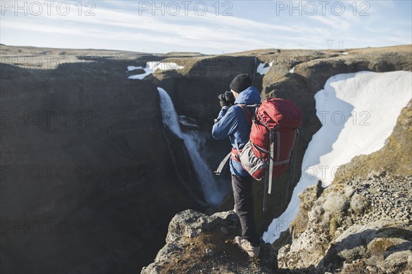 Hiker with backpack on cliff by Haifoss waterfall in Iceland