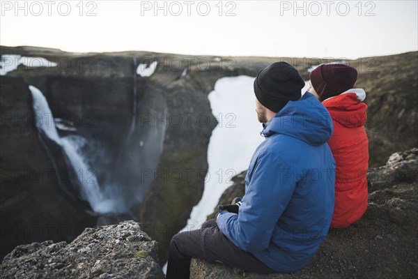 Hiker couple sitting on cliff by Haifoss waterfall in Iceland