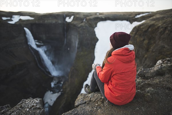 Hiker sitting on cliff by Haifoss waterfall in Iceland