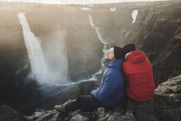 Hiker couple sitting on cliff by Haifoss waterfall in Iceland